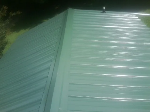 New green metal panels meeting at the ridge of a roof — Flat Roof Repair work by our crew in Martinsville