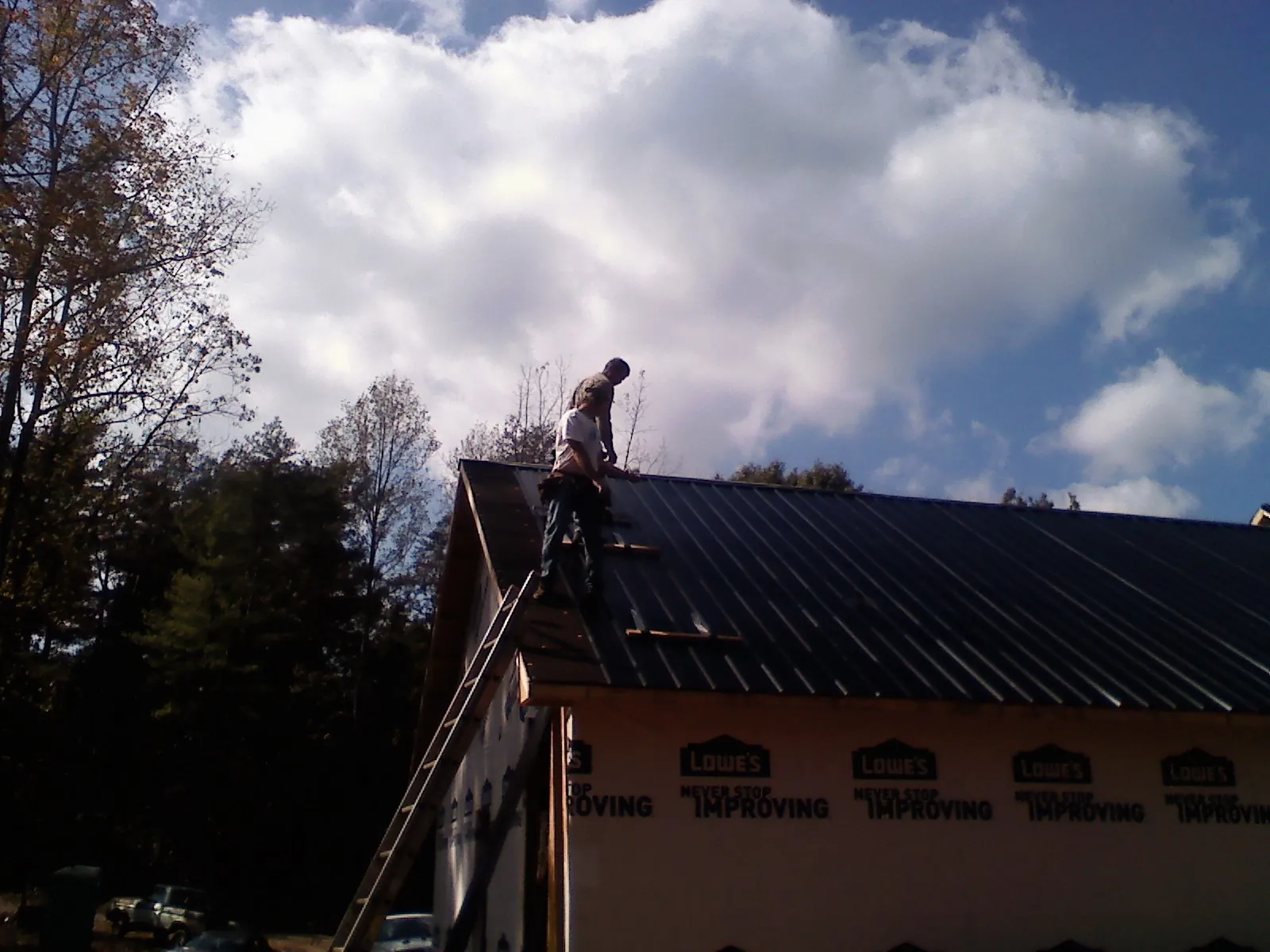Roofer fastening dark metal panels high against a cloudy sky, from a Roof Inspection job in Martinsville