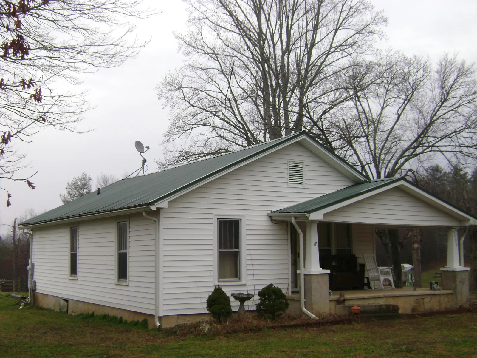 Green metal roof on a white bungalow with a side porch in Martinsville
